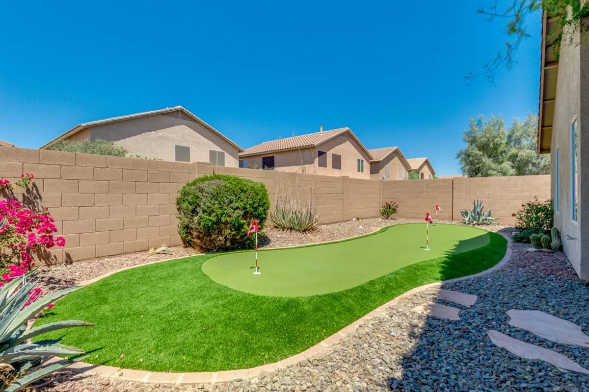 This image captures a well-maintained private putting green surrounded by flowering plants and a neat rock pathway. The playful, inviting mood makes it ideal for golf practice or quiet relaxation, with the landscaping reinforcing the outdoor leisure theme.