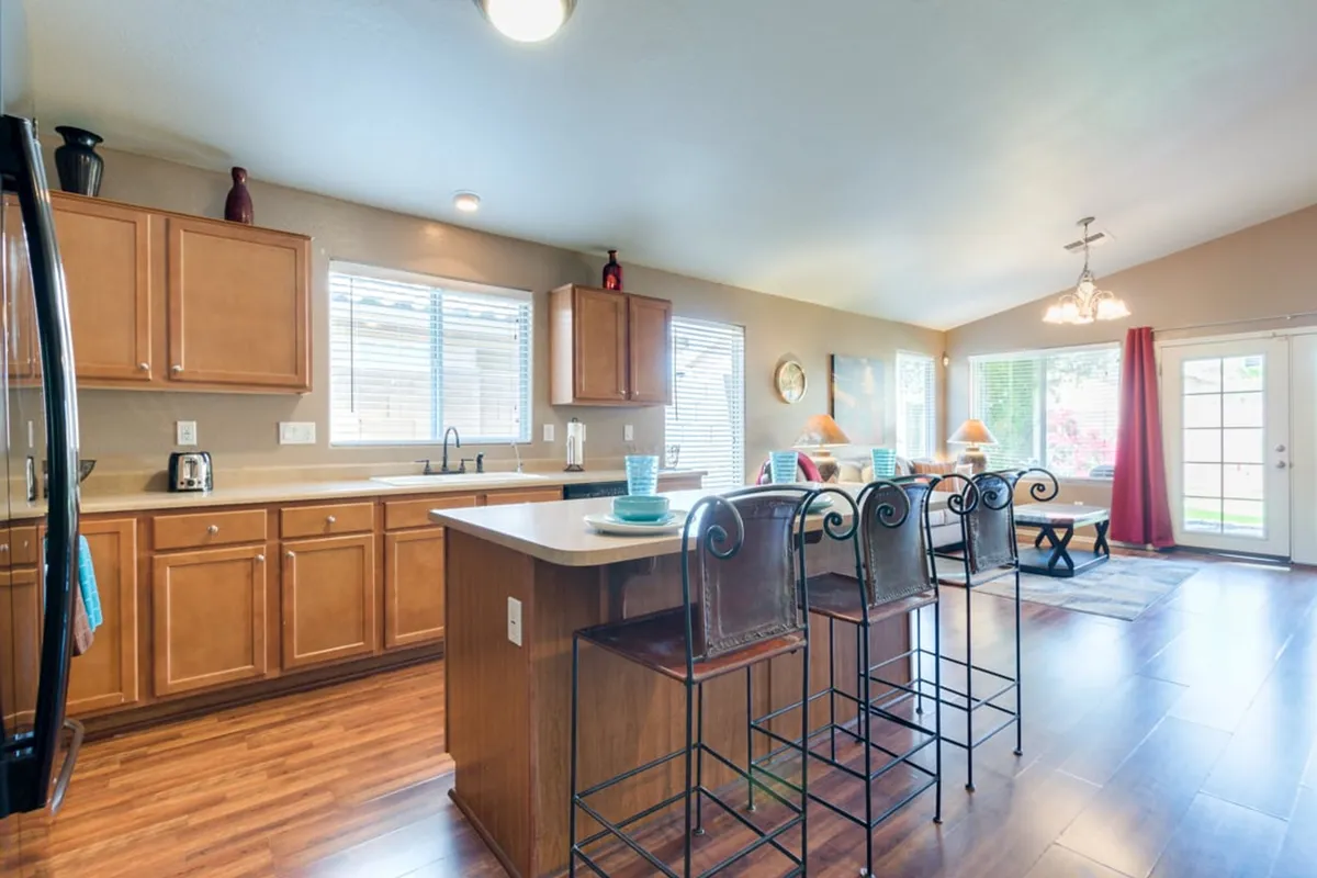 A bright kitchen with a large island, bar stools, and a sliding glass door that leads outside, filled with natural light and designed for both cooking and family gatherings.