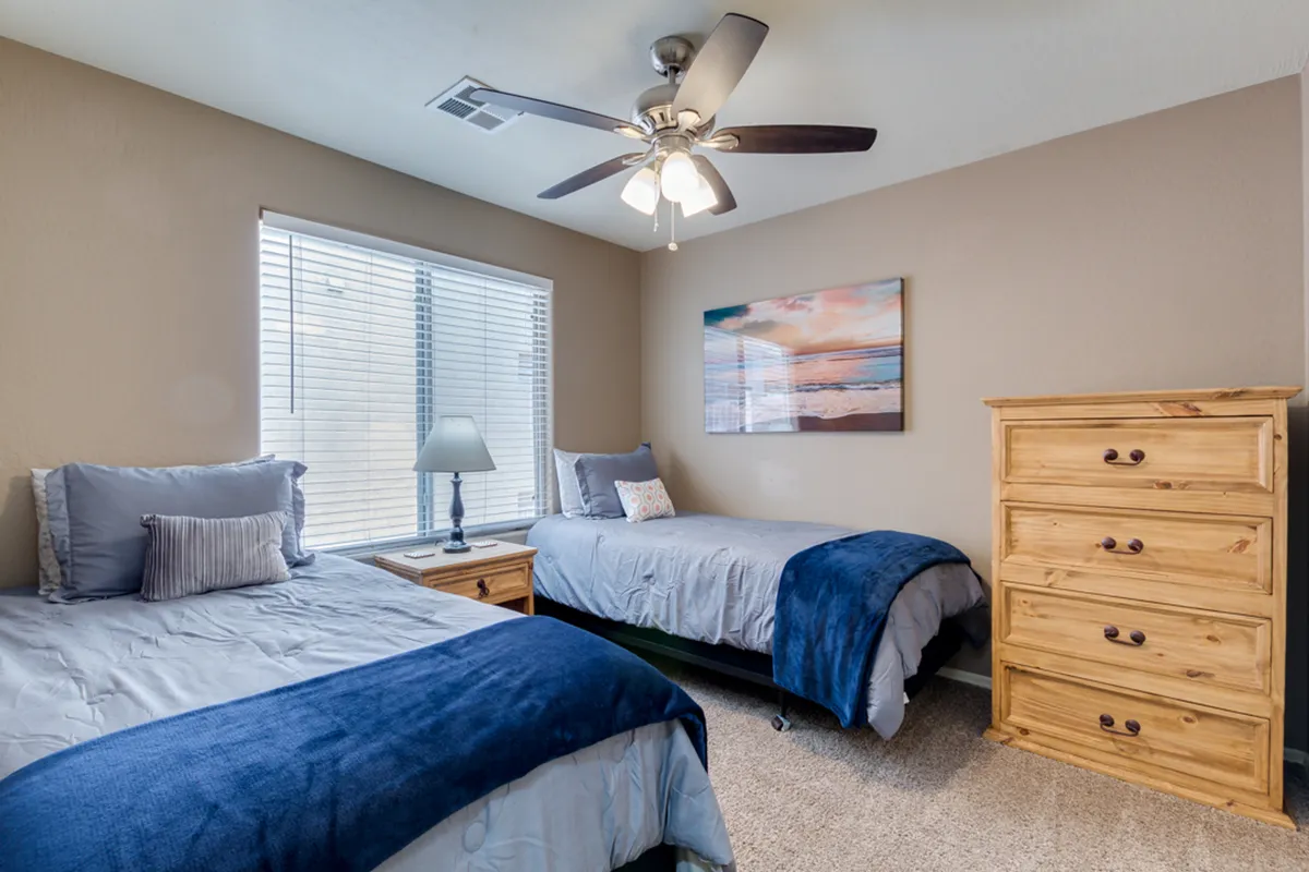A cozy bedroom with two twin beds, a wooden dresser, and cheerful wall art, offering a comfortable space ideal for children or friends sharing a room.