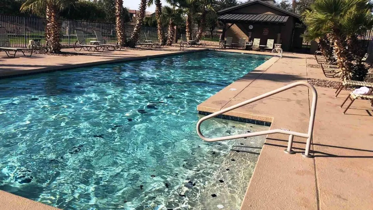 A sparkling outdoor swimming pool with inviting lounge chairs arranged along the deck, shaded by swaying palm trees. The pool area looks clean, modern, and perfect for relaxation or social gatherings, evoking a classic resort-style atmosphere.