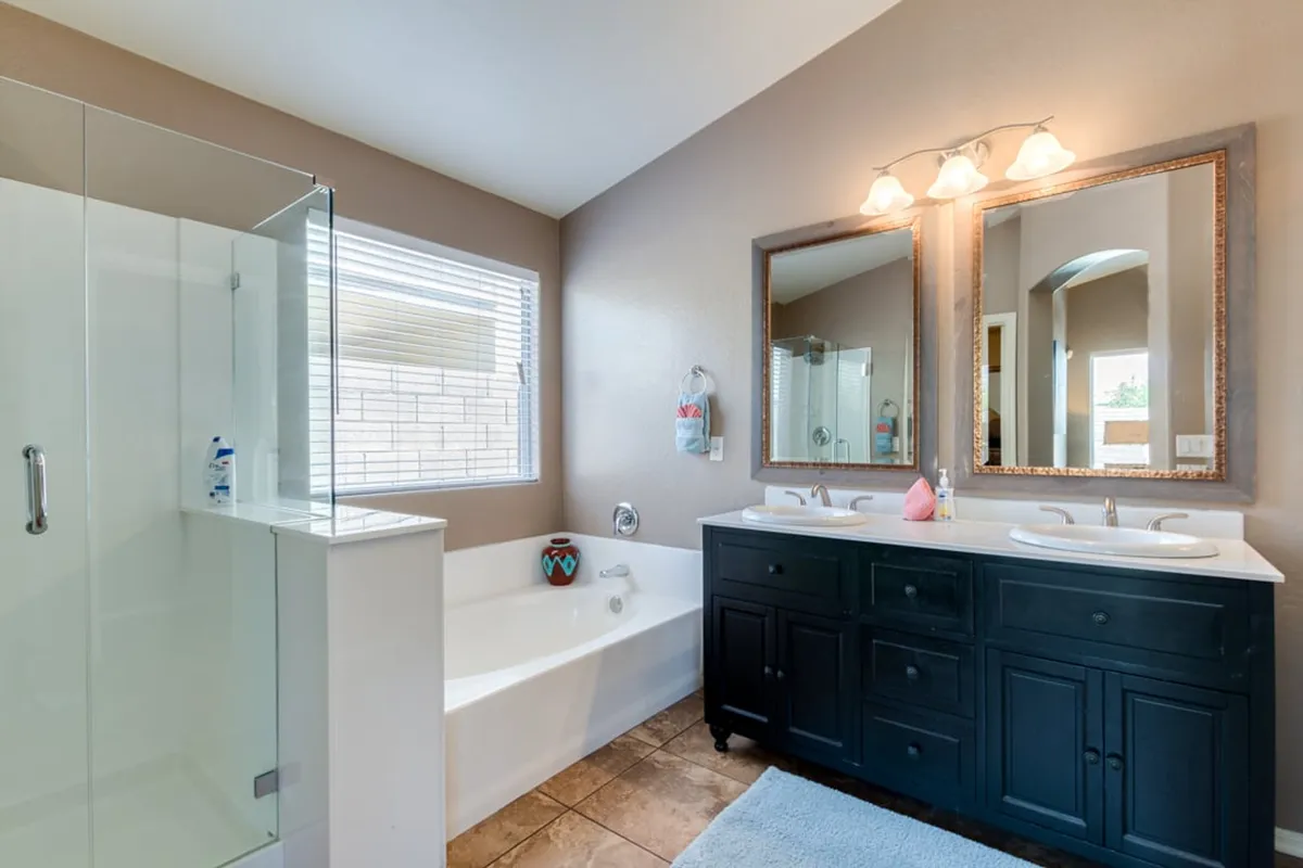 A spa-inspired bathroom with dual sinks, large mirrors, a relaxing bathtub, and a glass-enclosed shower—bathed in clean, natural light for a luxurious experience.